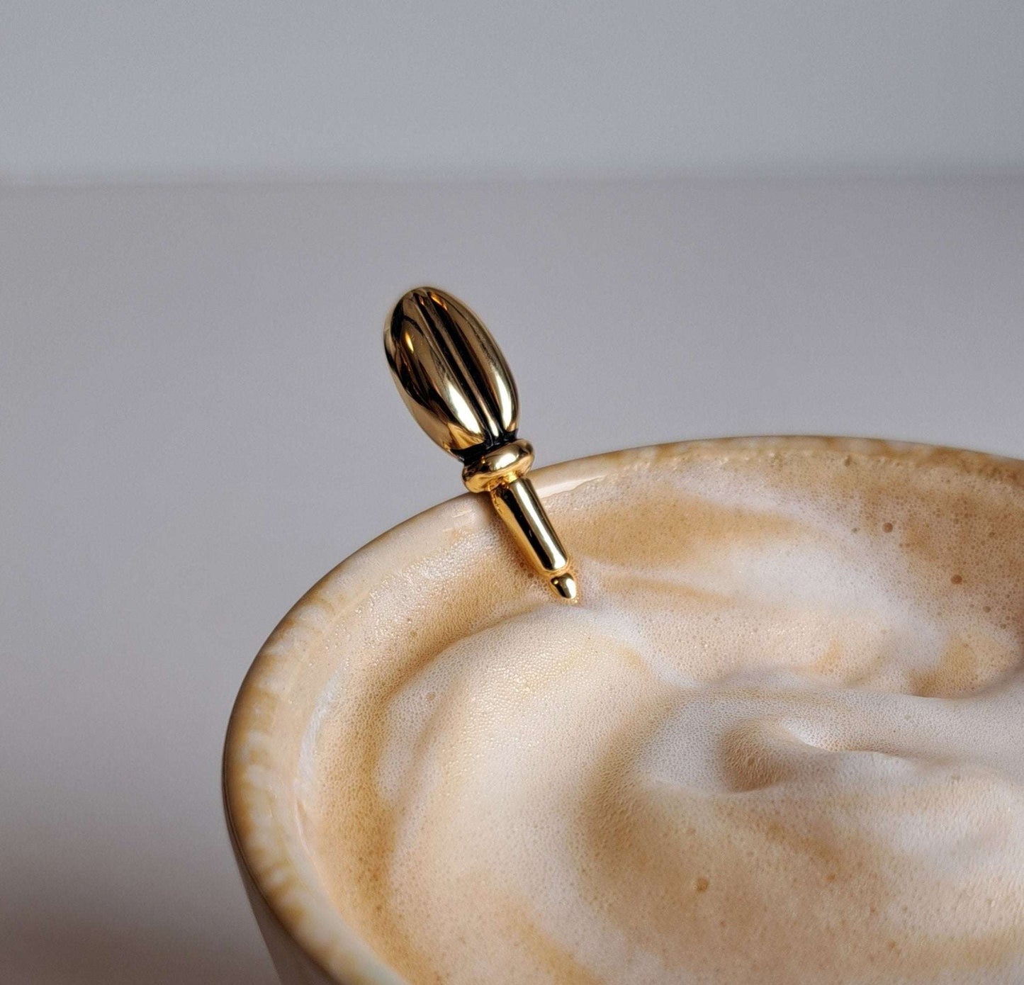 Goudkleurige koffielepel met detail van koffieboontje in een cappuccino
