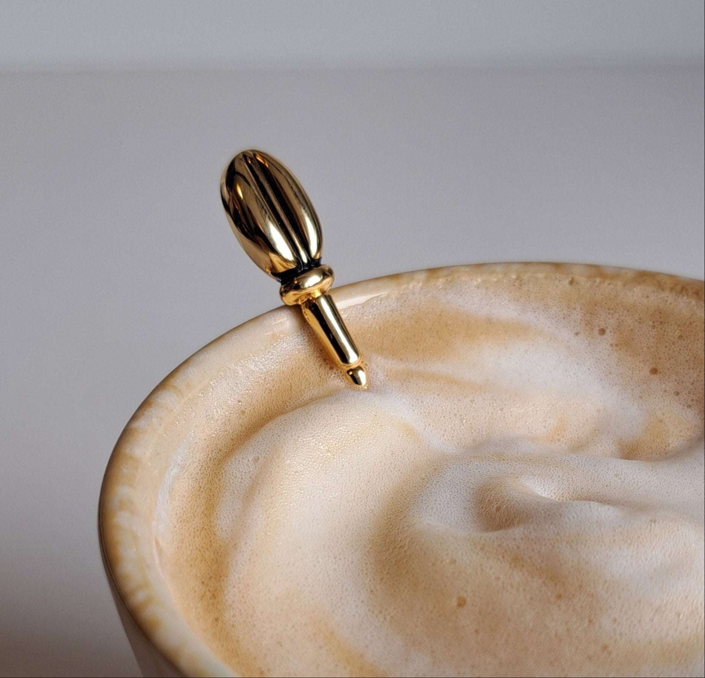 Goudkleurige koffielepel met detail van koffieboontje in een cappuccino