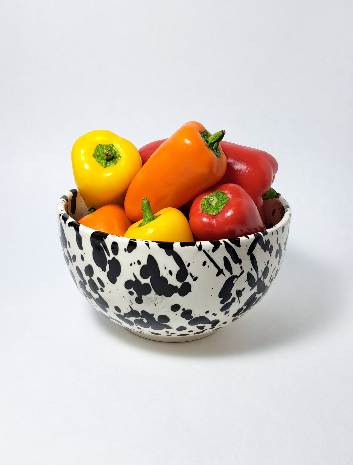 Tierra Cocida handgemaakte kom 14cm witte basis met zwarte glazuurspetters, gevuld met paprika's als sfeerbeeld